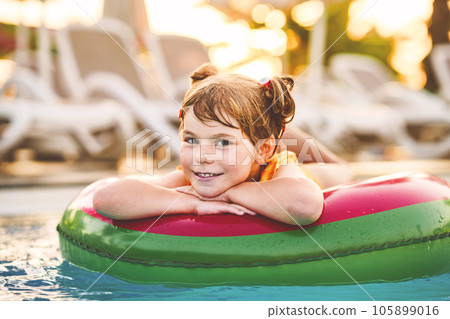Happy little girl with inflatable toy ring float in swimming pool. Little preschool child learning to swim and dive in outdoor pool of hotel resort. Healthy sport activity and fun for children. 105899016