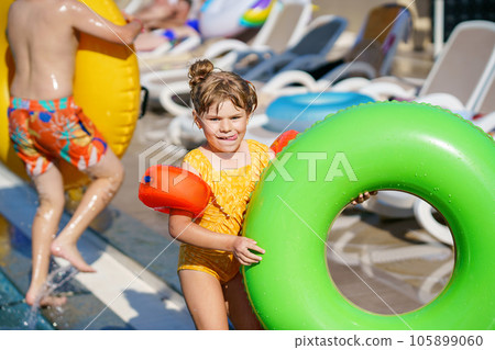Happy little girl with inflatable toy ring float in swimming pool. Little preschool child learning to swim and dive in outdoor pool of hotel resort. Healthy sport activity and fun for children. 105899060
