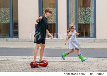 Little toddler girl running. School kid boy on hover board . Two happy children having fun with modern move gadgets, outdoor activity. Happiness, childhood. Excercise for kids. 105899064
