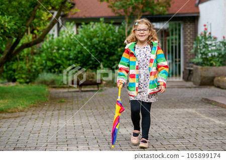 Little girl on way to elementary school or kindergarden. Preschool Child with colorful rainbow umbrella and waterproof jacket with school bag. Kid walking in autumn shower. Outdoor fun by any weather Little girl on way to elementary school or kindergarden. Preschool Child with colorful rainbow umbrella and waterproof jacket with school bag. Kid walking in autumn shower. Outdoor fun by any weather 105899174
