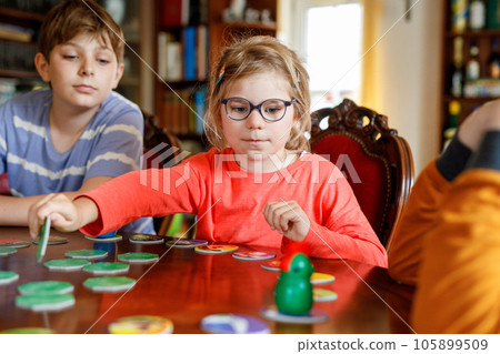 Family playing board game at home. Kids play strategic game. Little sister girl and two school brothers boys. Fun indoor activity. Siblings bond. Educational toys. Family playing board game at home. Kids play strategic game. Little sister girl and two school brothers boys. Fun indoor activity. Siblings bond. Educational toys. 105899509