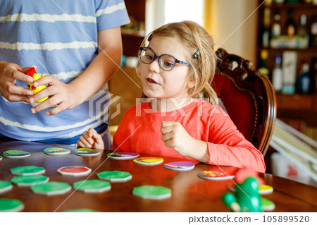 Family playing board game at home. Kids play strategic game. Little sister girl and school brother boy. Fun indoor activity. Siblings bond. Educational toys. Family playing board game at home. Kids play strategic game. Little sister girl and school brother boy. Fun indoor activity. Siblings bond. Educational toys. 105899520