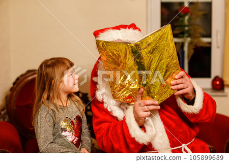 Little toddler girl talking to Santa Claus called Nikolaus or Weihnachtsmann in German. Happy smiling kid waiting for gifts. Santa with golden book. Xmas, childhood, holiday 105899689