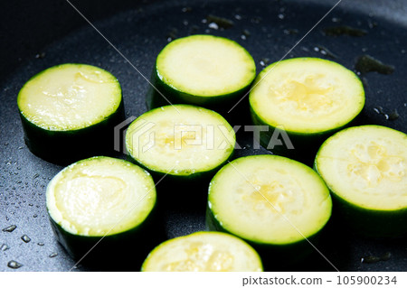 A cooking scene where round slices of zucchini are baked in a frying pan. A cooking scene where round slices of zucchini are baked in a frying pan. 105900234