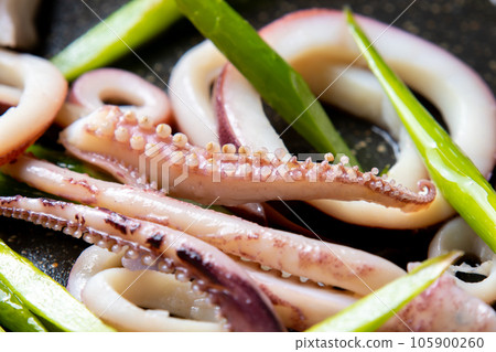 A close-up of a cooking scene in which squid (boiled squid) and garlic sprouts are fried in a frying pan. 105900260