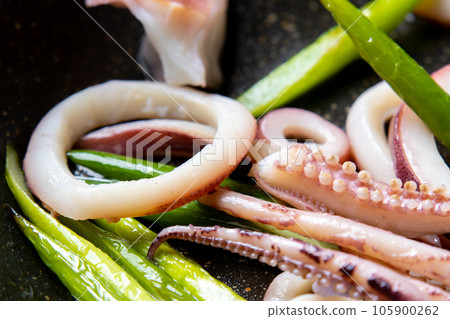 A close-up of a cooking scene in which squid (boiled squid) and garlic sprouts are fried in a frying pan. 105900262