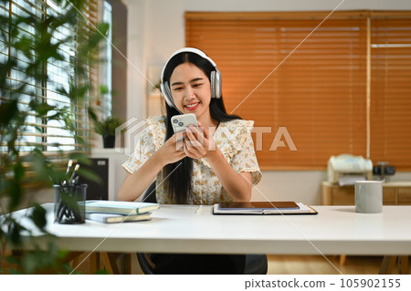 Pleasant young woman wearing headphones texting messaging, communication in social media on smartphone Pleasant young woman wearing headphones texting messaging, communication in social media on smartphone 105902155