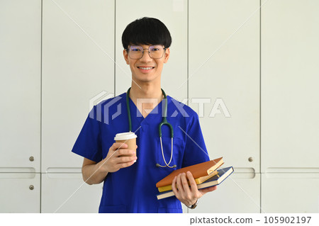 Smiling asian male medical student man wearing blue scrubs standing near window and looking at camera Smiling asian male medical student man wearing blue scrubs standing near window and looking at camera 105902197