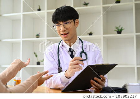 Smiling male general practitioner in white medical uniform giving consultation, explaining treatment to female patient 105902217
