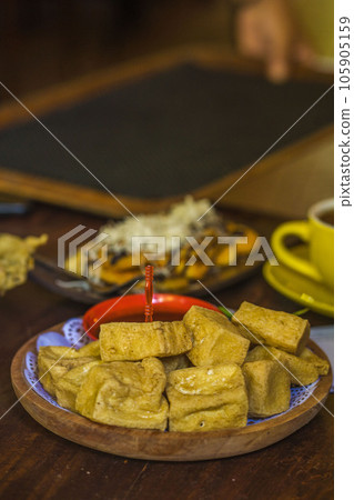 Assorted fried tofu, fried tempeh and banana fritters on the plate served with coffee on the table in a cafe in Blitar, East Java, Indonesia Assorted fried tofu, fried tempeh and banana fritters on the plate served with coffee on the table in a cafe in Blitar, East Java, Indonesia 105905159