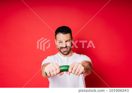 Young man in white shirt isolated over background. Guy look at long cucumber in hand. 105906843