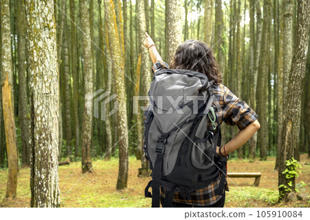 Rear view of an Asian woman trekking in the forest while pointing to something 105910084