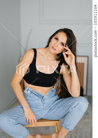 Sensual young stylish brunette with long hair in casual style, b in jeans, black knitted top, sitting on a stool in a cozy living room Sensual young stylish brunette with long hair in casual style, b in jeans, black knitted top, sitting on a stool in a cozy living room 105911104