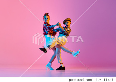 Beautiful, artistic, emotive children in retro stylish clothes dancing against pink studio background in neon light 105911581