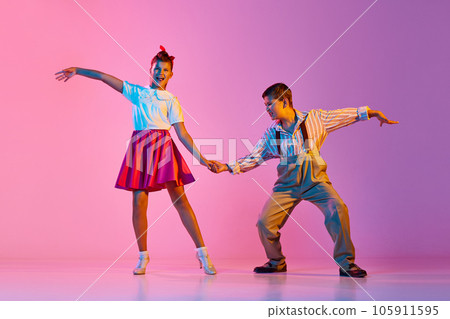 Talented, artisitc children, boy and girl in retro clothes dancing lindy hop against pink studio background in neon light 105911595