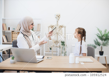 Physician consulting little girl using skeleton in hospital 105912524
