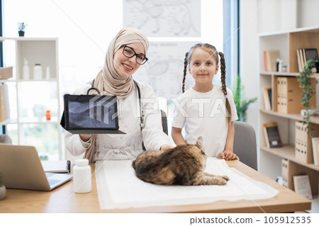 Vet with MRI on tablet and girl posing near desk with cat Vet with MRI on tablet and girl posing near desk with cat 105912535