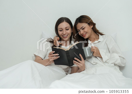 Two Asian cheerful happy female girlfriends having a coffee sitting on the bed while looking at the book. Concept lifestyle lesbian couple Two Asian cheerful happy female girlfriends having a coffee sitting on the bed while looking at the book. Concept lifestyle lesbian couple 105913355