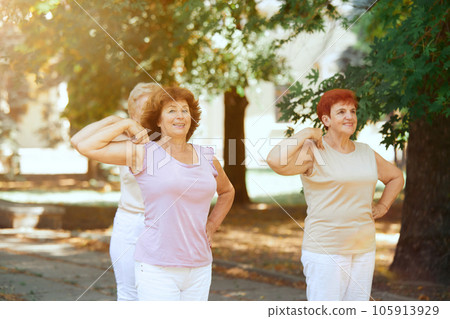 Senior sportive woman training together outdoors on warm summer morning. Stretching and warming up exercises Senior sportive woman training together outdoors on warm summer morning. Stretching and warming up exercises 105913929