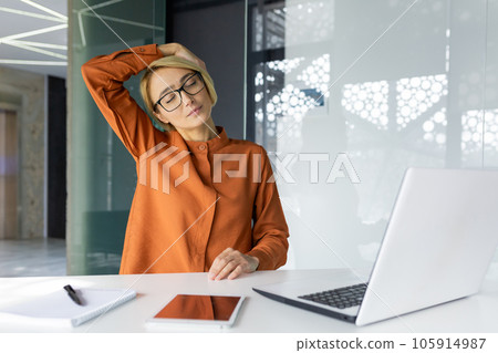 Businesswoman tired at workplace, long sitting work inside office, sick woman has severe neck pain, working at laptop while sitting. Businesswoman tired at workplace, long sitting work inside office, sick woman has severe neck pain, working at laptop while sitting. 105914987