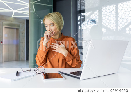 Sick cold woman at workplace, coughing, businesswoman sitting at desk with laptop inside office. Sick cold woman at workplace, coughing, businesswoman sitting at desk with laptop inside office. 105914990