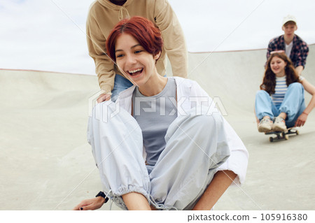 Close-up of smiling, laughing, positive teen girl spending good time with friends on skate park, skateboarding 105916380