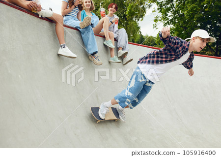 Friends, teengaers meeting at skate park for active leisure time. Boy in casucl clothes skateboarding on ramp Friends, teengaers meeting at skate park for active leisure time. Boy in casucl clothes skateboarding on ramp 105916400