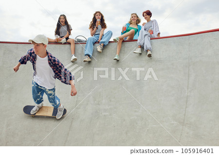 Teen boy in casual sport style clothes skateboarding on outdoor skate park. Friends meeting together on warm summer day 105916401