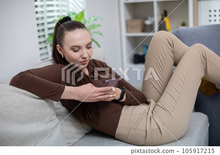 Girl uses cell phone while sitting on couch Girl uses cell phone while sitting on couch 105917215