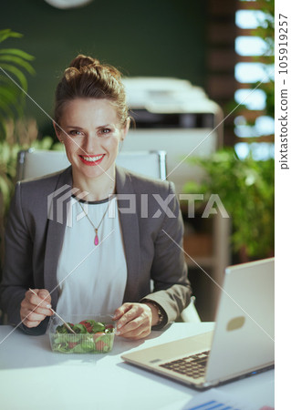happy 40 years old business woman in green office eating salad 105919257