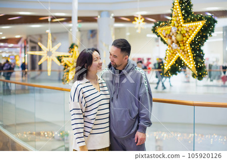 young Asian Kazakh couple, man and woman look at each other with love in Christmas shopping mall. newlyweds, young family. portrait young Asian Kazakh couple, man and woman look at each other with love in Christmas shopping mall. newlyweds, young family. portrait 105920126