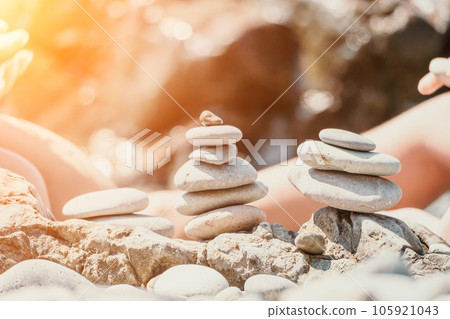 Woman with daughter bilds stones pyramid on seashore on a sunny day on the blue sea background. Happy family holidays. Pebble beach, calm sea. Concept of happy vacation on the sea, meditation, spa Woman with daughter bilds stones pyramid on seashore on a sunny day on the blue sea background. Happy family holidays. Pebble beach, calm sea. Concept of happy vacation on the sea, meditation, spa 105921043