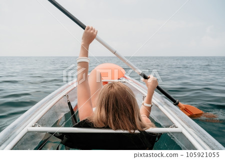 Woman in kayak back view. Happy young woman with long hair floating in transparent kayak on the crystal clear sea. Summer holiday vacation and cheerful female people relaxing having fun on the boat 105921055