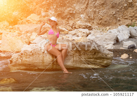 Woman travel sea. Woman traveler captures sea memory in pink bikini, posing on beach amidst volcanic mountains for adventurous journey. Happy tourist enjoys outdoor photography. Woman travel sea. Woman traveler captures sea memory in pink bikini, posing on beach amidst volcanic mountains for adventurous journey. Happy tourist enjoys outdoor photography. 105921117
