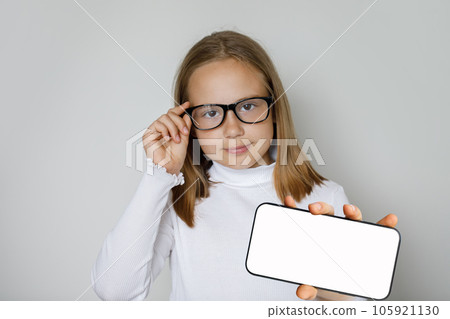 Portrait of young clever girl in glasses showing smart phone with big blank empty white display  105921130