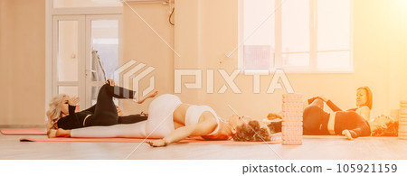 Happy middle aged well looking women, performing fascia exercises on floor using massage foam roller - tool to relieve tension in the back and relieve muscle pain. Female fitness yoga routine concept Happy middle aged well looking women, performing fascia exercises on floor using massage foam roller - tool to relieve tension in the back and relieve muscle pain. Female fitness yoga routine concept 105921159