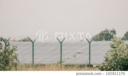 Large solar station with blue photovoltaic panels fenced with lattice and barbed wire. Producing clean energy from the sun and minimizing the carbon footprint. Large solar station with blue photovoltaic panels fenced with lattice and barbed wire. Producing clean energy from the sun and minimizing the carbon footprint. 105921170