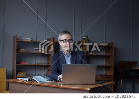 Portrait of mature attractive businessman in suit pensivly doing his work on the laptop in office 105921675