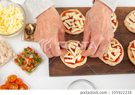 Adding toppings to the mini pizzas. Adding cheese. Delicious homemade mini pizzas preparation. Adding toppings to the mini pizzas. Adding cheese. Delicious homemade mini pizzas preparation. 105922216
