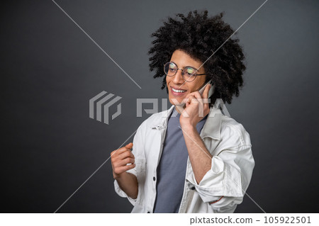 Young curly-haired guy talking on the phone and looking contented Young curly-haired guy talking on the phone and looking contented 105922501