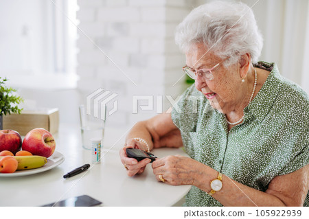 Diabetic senior patient checking her blood sugar level with fingerstick testing glucose meter. 105922939
