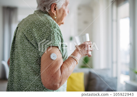 Diabetic senior patient using continuous glucose monitor to check blood sugar level at home. 105922943