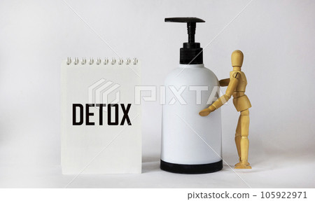 Word DETOX on notepad and white background, detox concept. There is a wooden doll with a dispenser 105922971