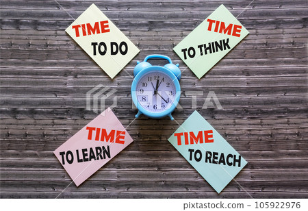 Texts on stickers about time on a wooden table with an alarm clock. 105922976