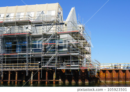 Reconstruction works of a house built on metal piles by the water, scaffolding around the facade Reconstruction works of a house built on metal piles by the water, scaffolding around the facade 105923501