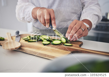 Cut, cucumber and hands cooking vegetable in a kitchen on a board or table in a home for hygiene as a chef. Salad, food and person prepare produce for a supper, lunch or dinner for diet meal Cut, cucumber and hands cooking vegetable in a kitchen on a board or table in a home for hygiene as a chef. Salad, food and person prepare produce for a supper, lunch or dinner for diet meal 105924525
