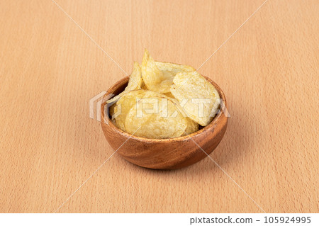 Thin potato chips in a bowl over a wooden background. 105924995