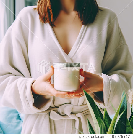 Beautiful young lady dressed in white home dress holding jar of cosmetic cream in her hands, beauty product container mockup Beautiful young lady dressed in white home dress holding jar of cosmetic cream in her hands, beauty product container mockup 105926547