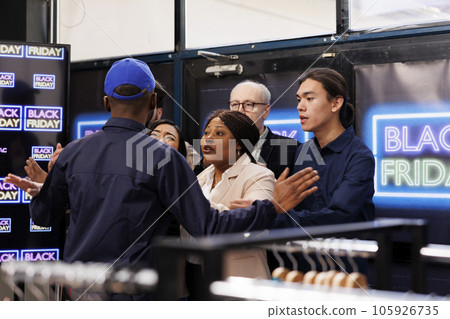 Agressive diverse people shoppers arguing with security guy at clothing shop entrance, waiting in line for Black Friday deals on Thanksgiving. Bargan hunters racing to store in search of holiday deals Agressive diverse people shoppers arguing with security guy at clothing shop entrance, waiting in line for Black Friday deals on Thanksgiving. Bargan hunters racing to store in search of holiday deals 105926735