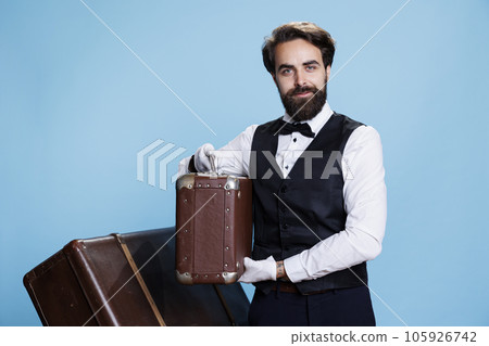 Charismatic bellhop with classic uniform, strikes confident pose against studio background. Professional doorkeeper expressing sense of reliability to provide excellent service and assistance. 105926742